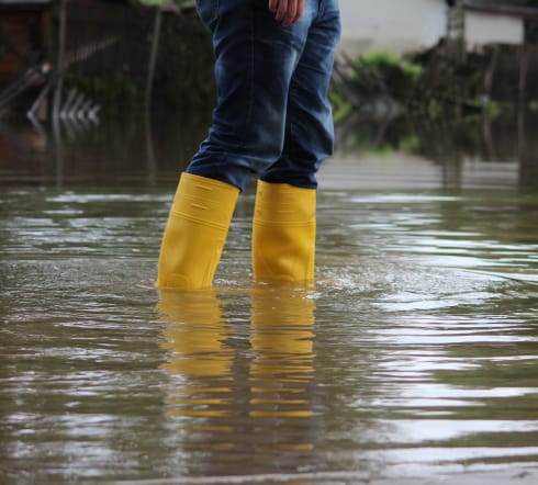 image of a person walking through a flooded area, glad at the fact they have flood insurance with the best inaurnace agency in Columbia, SC