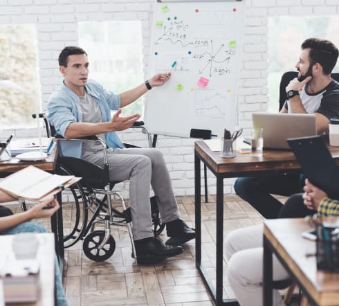 image of a man on a wheelchair pointing to a graph about Group Disability Insurance while two other man stare at what he's pointing at in a Columbia, SC office